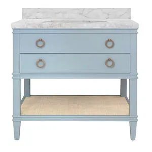 Soft blue wood bath vanity with single drawer, ring pull handles, marble countertop, porcelain sink, and open cane lower s...